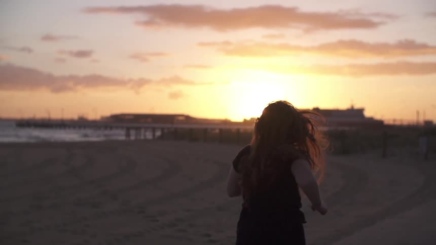 Woman running down a beach at sunset