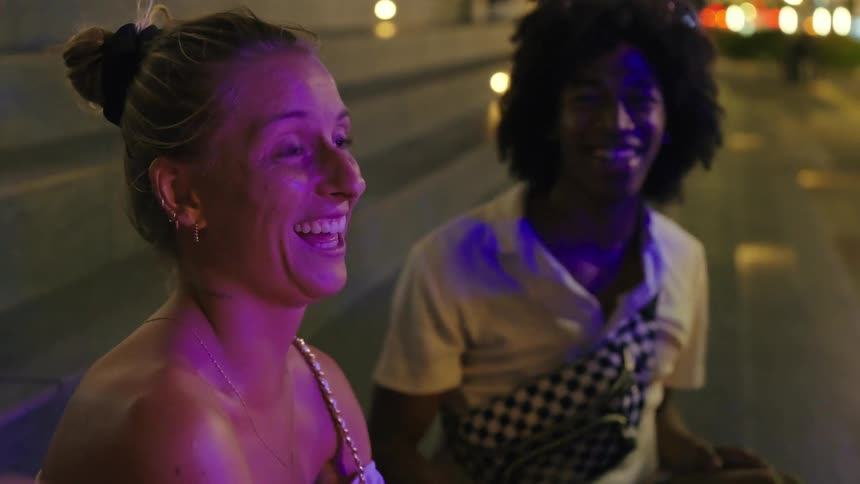 Three friends sitting on an outdoor staircase at night talking smiling