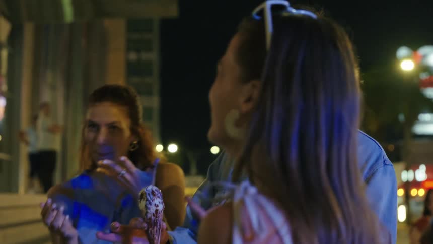 Friends eat ice cream on the sidewalk of a city street at night