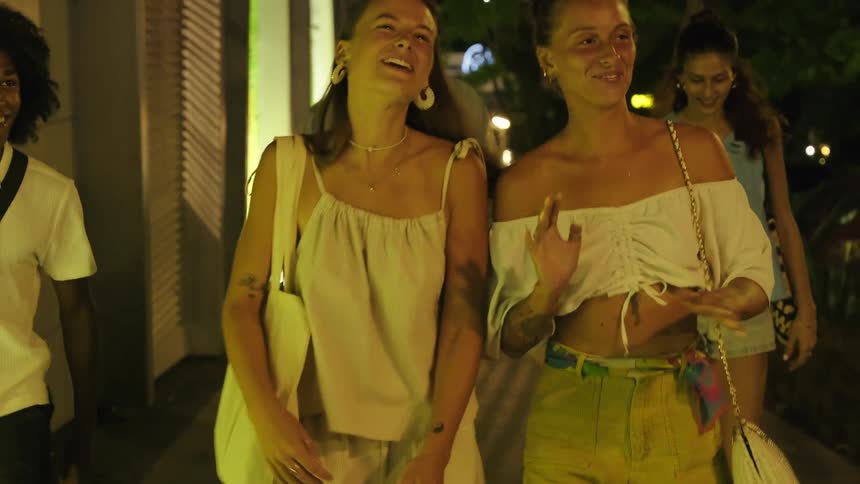 Friends laugh and talk while walking on a downtown sidewalk at night