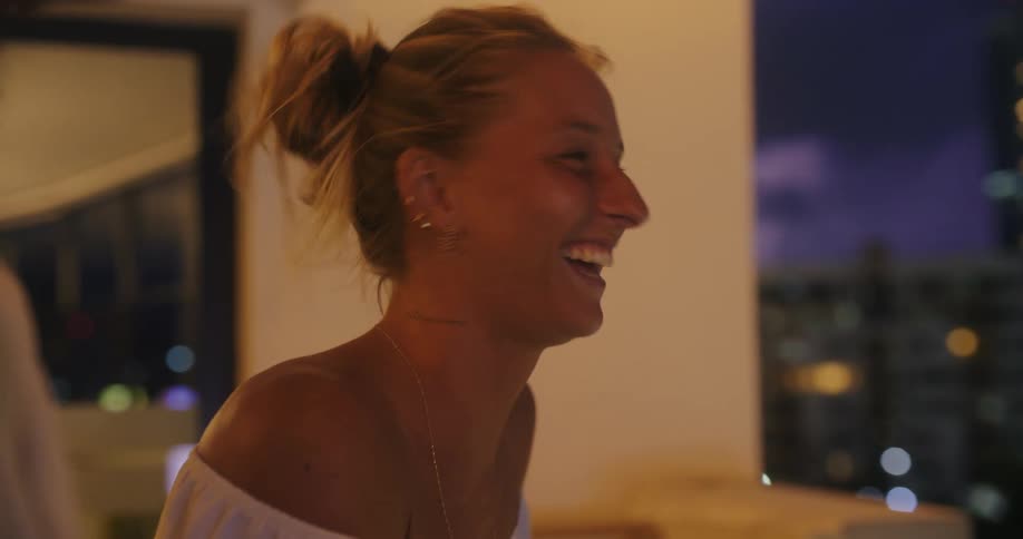 Woman smiling on a balcony at dusk with city lights in the background