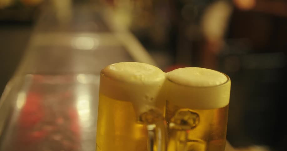 A hand pours beer into two frothy glasses at a bar