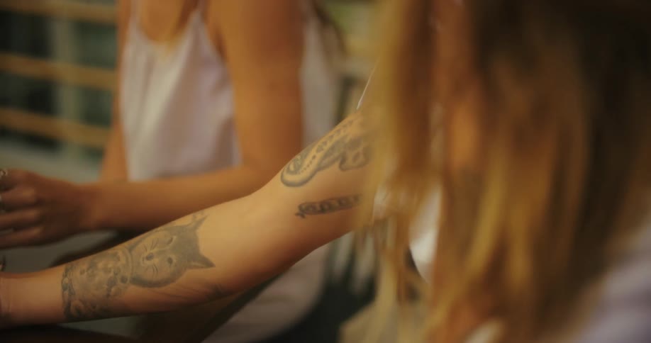A group of friends sit at a tables as one shows off the tattoos on her arm