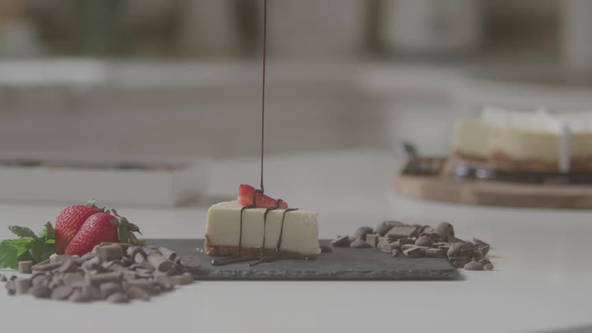Chocolate cream being poured over a cake on a table topped with a strawberry