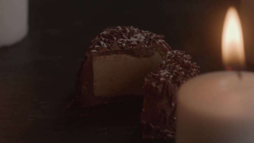 A chocolate dessert cut in half is placed beside a lit candle
