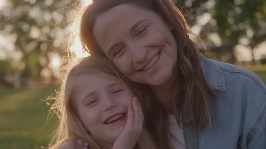 A woman and a young girl on a grass field smiling as they put their heads together for a photo