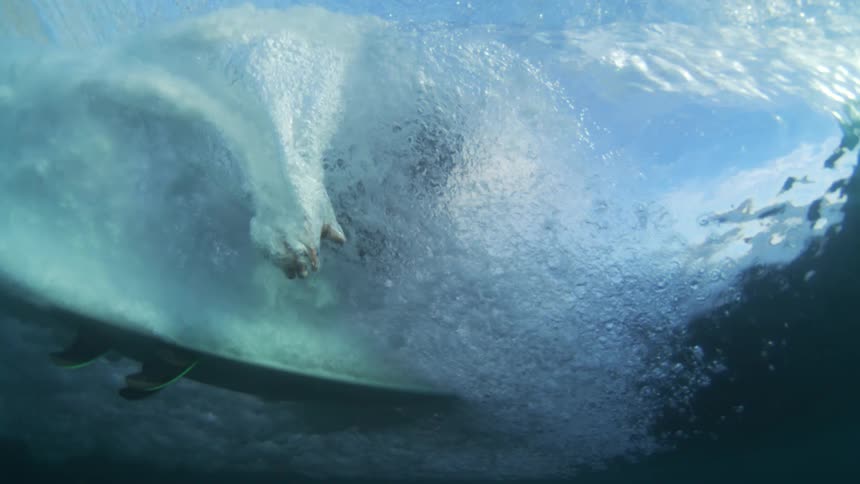 Churning of a crashing wave obscures the surfer briefly visible through it on a sunny day
