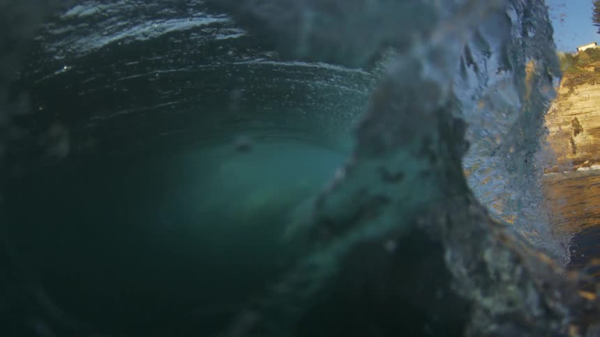 Ocean swell forms a clean barrel by rocky shore