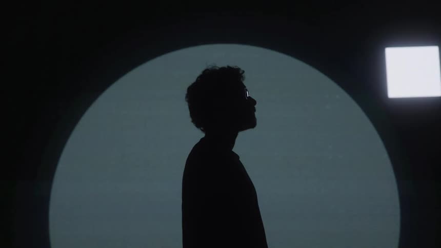 A lone profile stands against glowing circular shapes in a minimalist studio