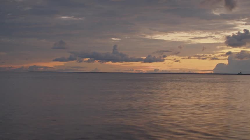 The sea sits calm beneath a muted sunset and slowmoving clouds