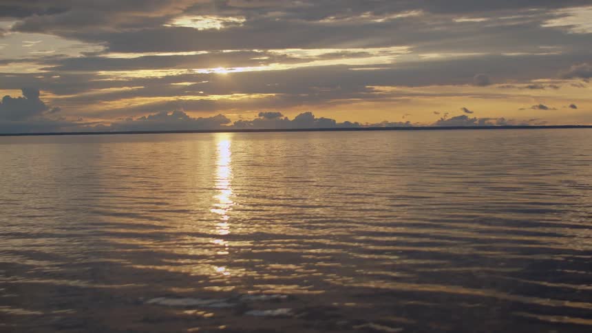Calm ocean reflects the golden sunset on the horizon