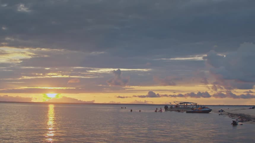 People swimming near boats during sunset at sea