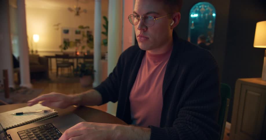 Man with glasses uses a laptop while working at a lit table