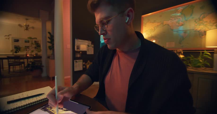 Man wearing glasses and earphones draws on a tablet with a stylus