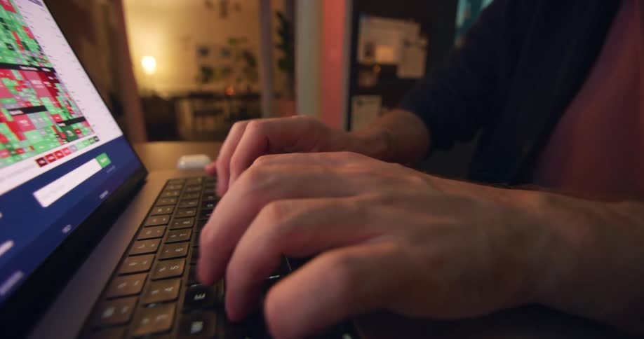 Closeup of hands typing on a laptop with a stock market screen visible