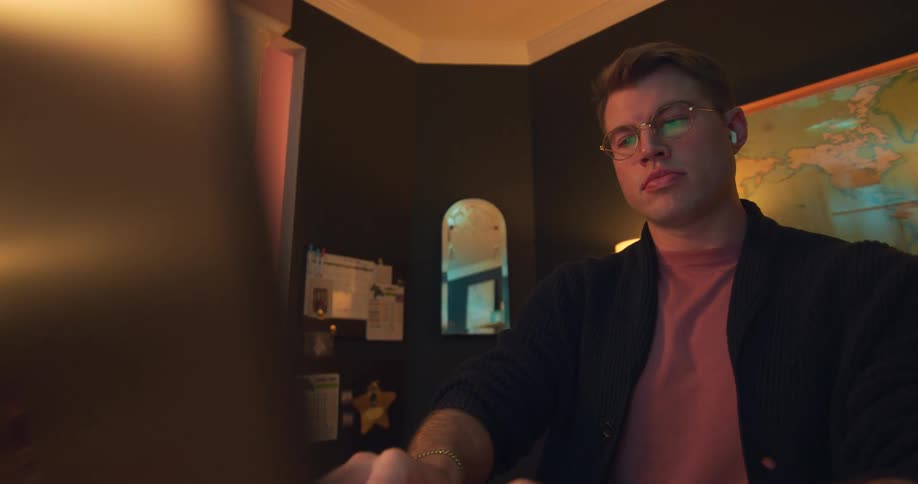 A man sits at a desk working on a laptop indoors