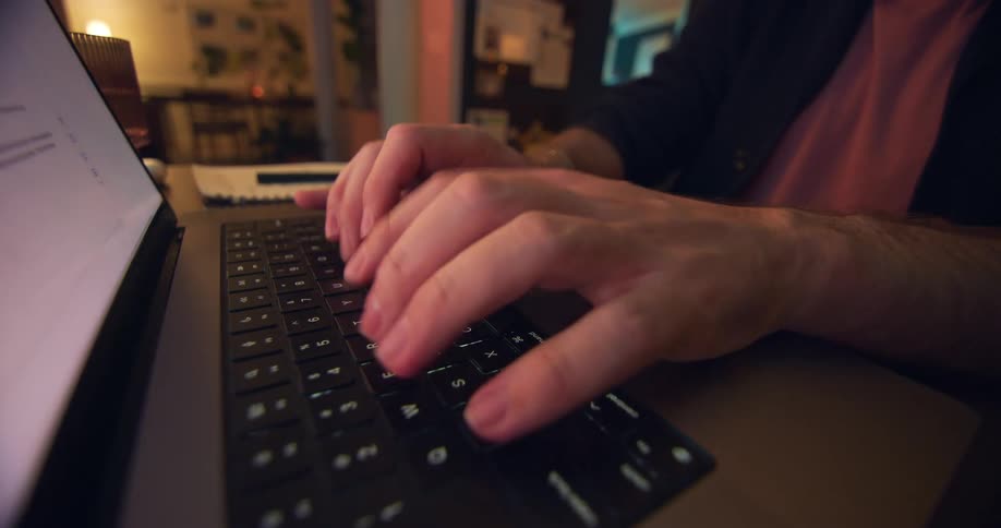 White male hands typing on a laptop keyboard indoors during