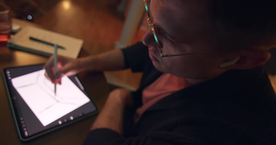 Close up of a young man drawing on a tablet computer while sitting at a table indoors