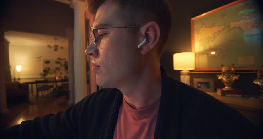 Man with glasses sitting putting on earbuds