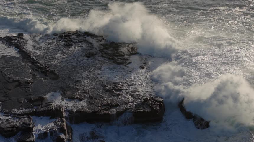 Waves crashing onto the rocks spray water into the air before covering the area with foam