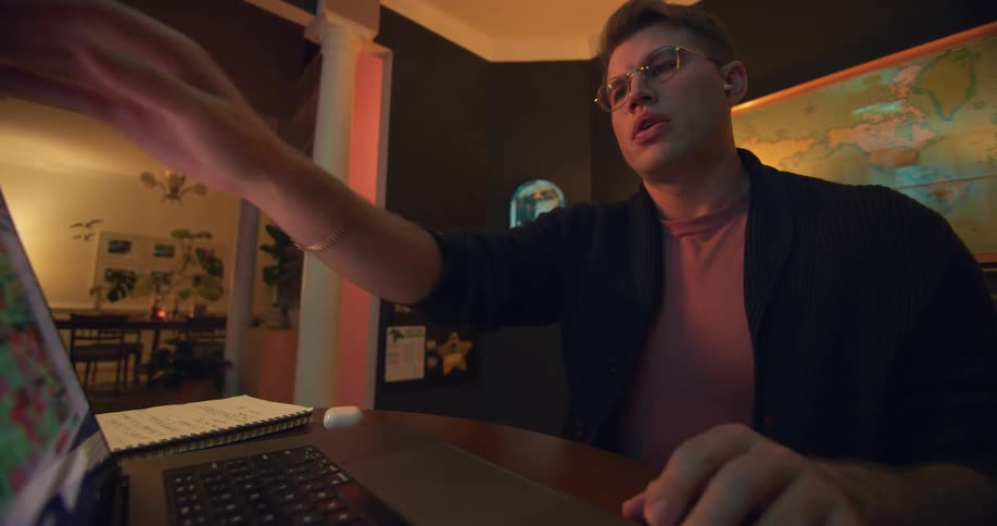 Young white man wearing glasses typing on a laptop computer and checking his smartphone indoors during day time