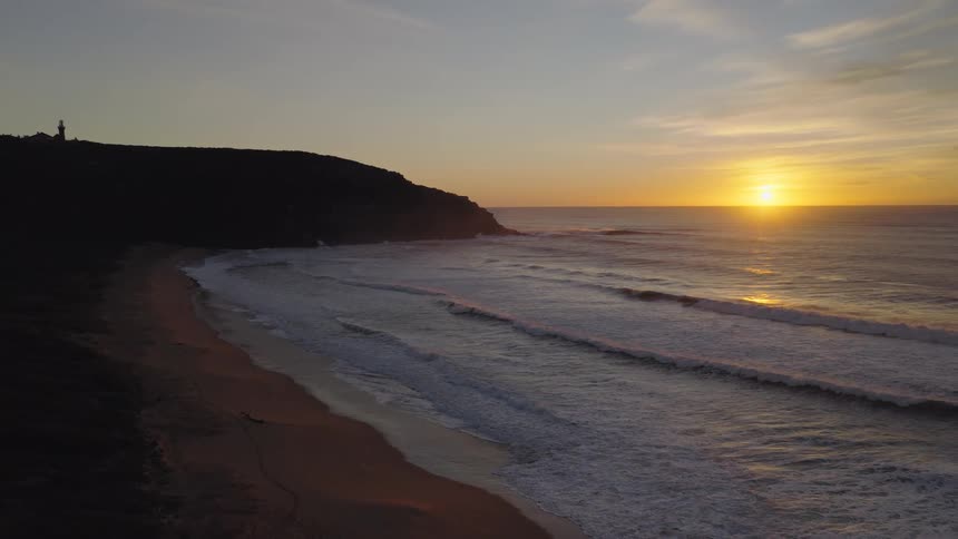 Sun sets over the sea lighting up the waves reaching the shore