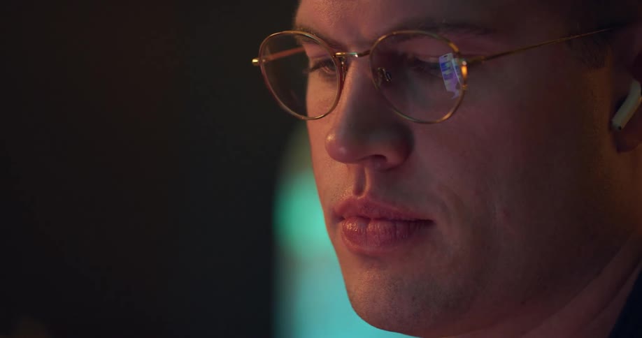 A man wearing glasses stares a computer screen while wearing air pods