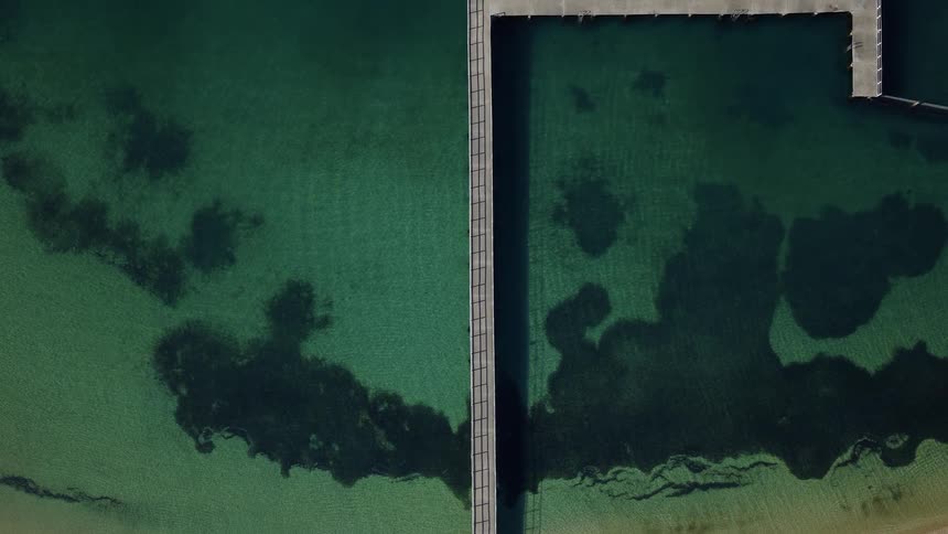 Walkway over green waters seen from above with dark shadows on the bottom