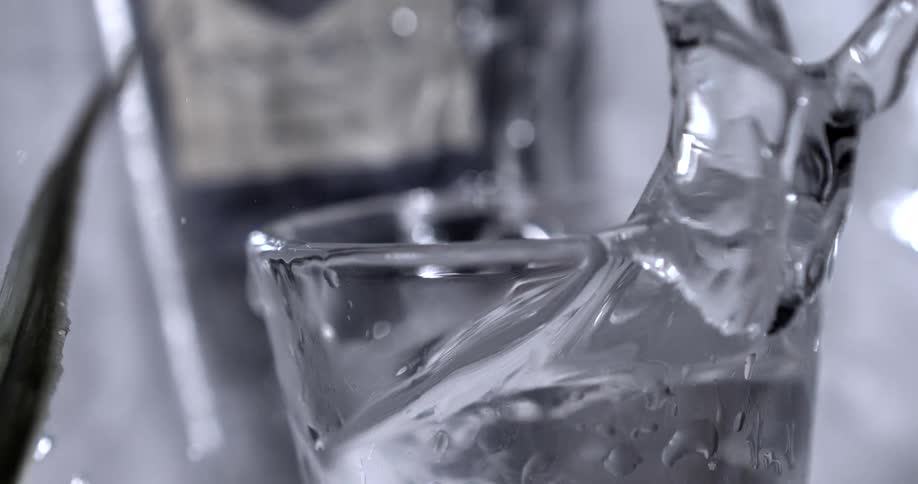 In an extreme closeup slowmotion shot an ice cube is dropped into a glass creating a dramatic splash that sends water everywhere