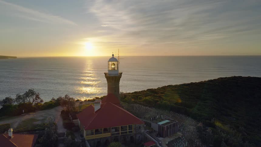 Building with a lighthouse stands near the coast as the sun rises on the horizon