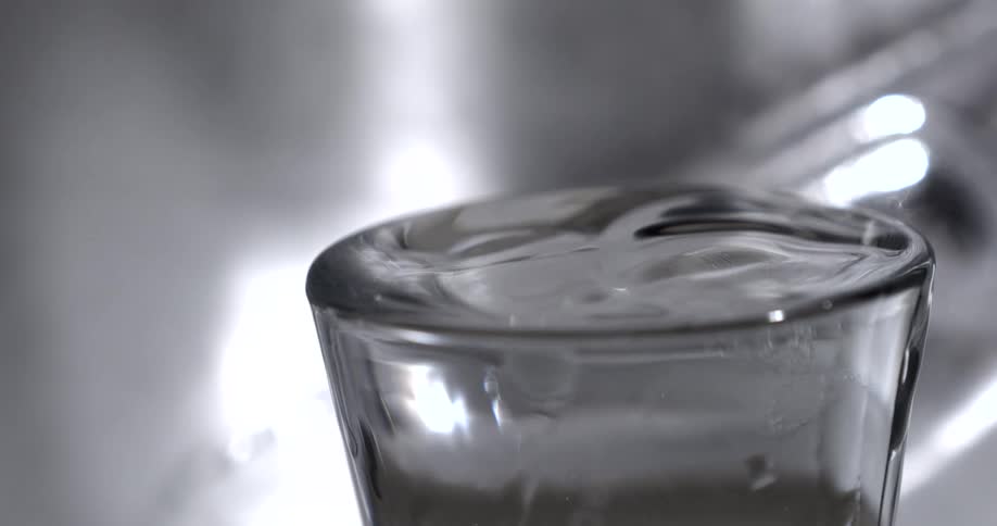 Close up of a water droplet falling into a glass cup filled with water