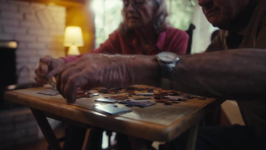 Two seniors collaborate over a jigsaw puzzle steady hands sorting pieces on a small table by the lamp