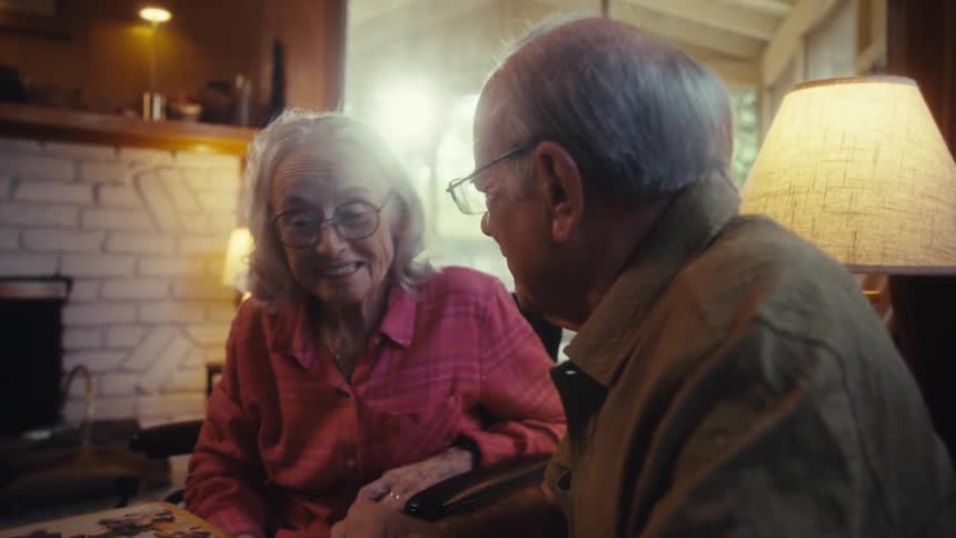 An elderly couple smiles while solving a puzzle at home