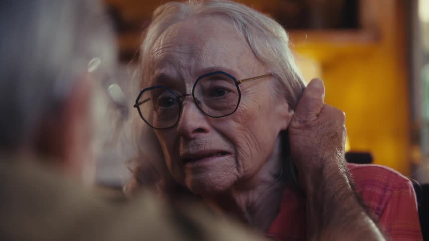Elderly woman smiling while talking to a man in a cozy setting