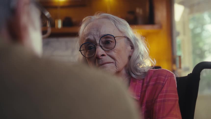 Elderly woman with glasses looks attentively at the person in front of her