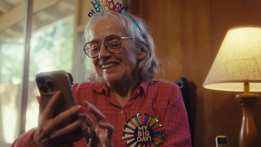 An elderly woman smiles while reading birthday wishes on her phone
