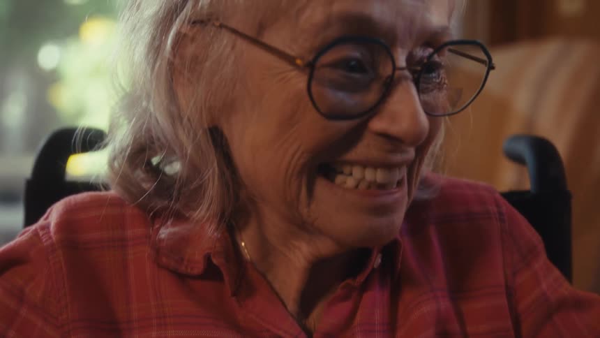 Smiling elderly woman holds gift wrapped in golden paper with white ribbon