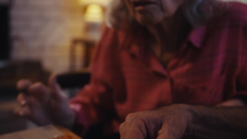 Elderly woman playing with a jigsaw puzzle sitting next to an elderly man indoors during day time