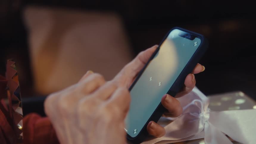 Elderly hands hold a smartphone next to a gift with a white ribbon