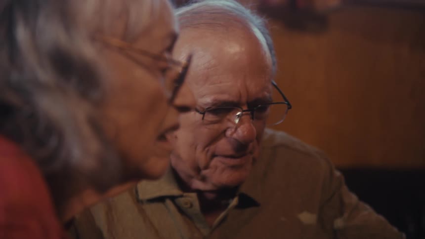 An older couple sit close together at a table sharing a quiet moment