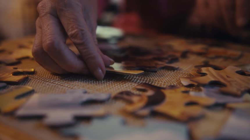 A persons hand placing a puzzle piece on a flat surface with several other pieces