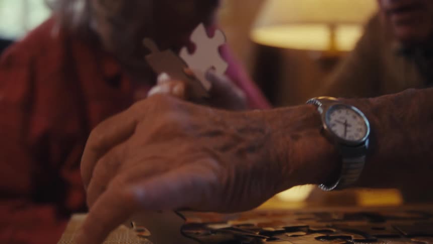 Elderly man and woman sitting down playing with a jigsaw puzzle and talking indoors
