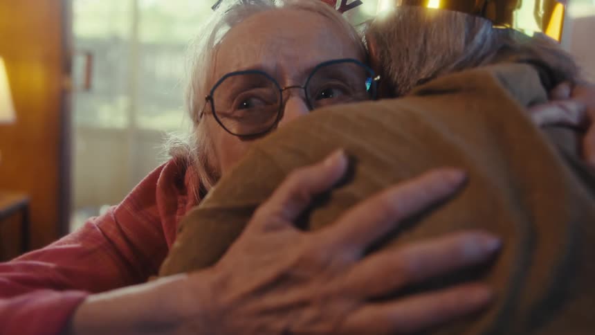 An elderly woman joyfully receives a wrapped birthday gift