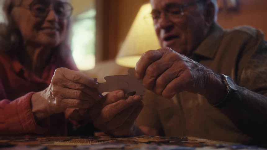 Elderly couple having fun buildng a puzzle on a tv tray