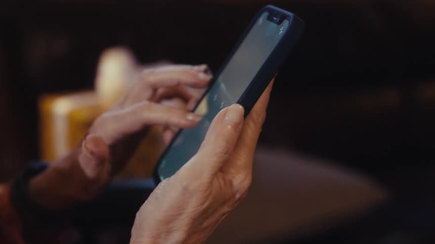 Elderly womans hands hold a smartphone while browsing the screen