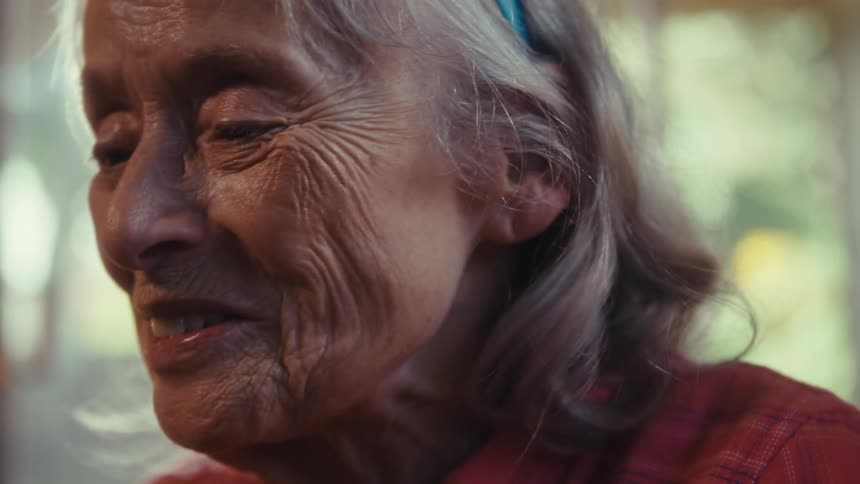 A grandmothers gentle smile catches warm sunlight as she talks while holding a cell phone