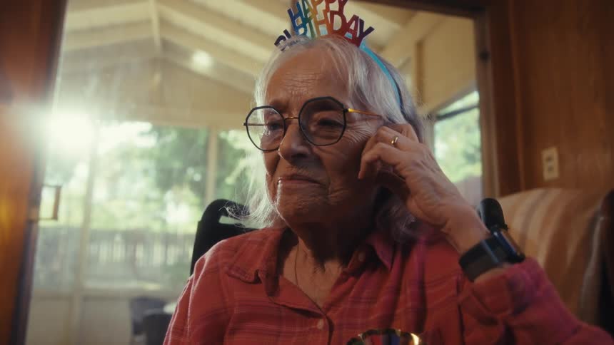 Close up portrait of an elderly woman using a mobile phone while sitting in a room indoors on her birthday