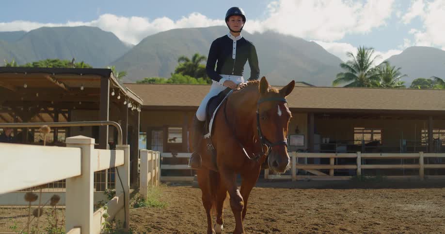 White woman wearing riding gear and riding a horse on a ranch outdoors during day time