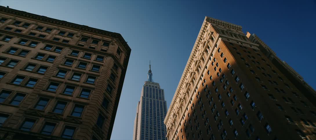 View looking up at the empire state building between tall buildings