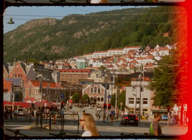 A vintageframed city street bustles with cars and pedestrians warm film burns edging a hillside of homes